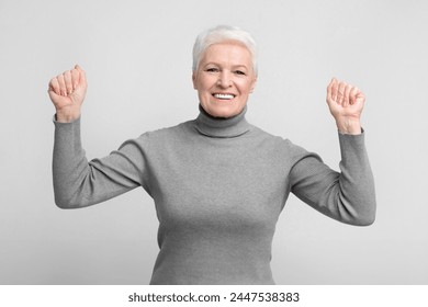 Cheerful senior european woman throws her fists up in a victory pose, ideal image for s3niorlife promotions