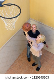 Cheerful Senior Family Couple Playing Basketball In Patio. Focus On Woman