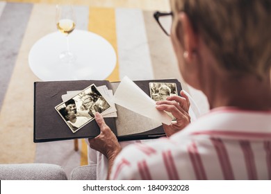 Cheerful senior female holding family photo album sitting on sofa at home