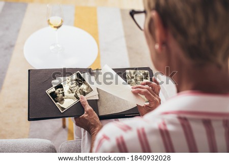 Cheerful senior female holding family photo album sitting on sofa at home