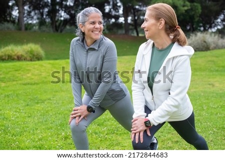 Cheerful senior friends exercising in park. Women in sportive clothes stretching on cloudy day. Sport, friendship concept