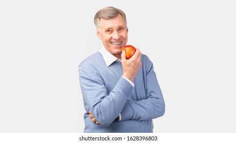 Cheerful Senior Gentleman Holding Apple Posing Over Gray Studio Background. Healthy Nutrition For Old People. Panorama - Powered by Shutterstock