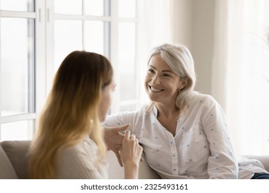 Cheerful senior grandma and teen granddaughter kid speaking on couch, laughing. Mature mom and adult daughter talking at home, enjoying conversation, bonding, affection - Powered by Shutterstock