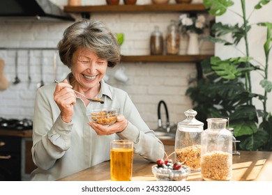 Cheerful senior grandmother eating cereals for breakfast mixing with berries drinking apple juice at home kitchen. Healthy dieting concept. Active seniors - Powered by Shutterstock