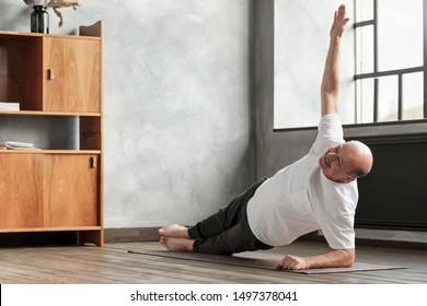 Cheerful senior hispanic man doing a side plank exercise at living room. Doing yoga at home at old age. - Powered by Shutterstock