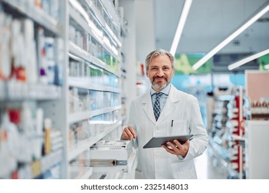 A cheerful senior male pharmacist doing a medical inventory, using a digital tablet and smiling for the camera. - Powered by Shutterstock