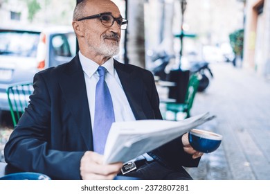 Cheerful senior man with grey beard in street cafe with coffee cup and newspaper - Powered by Shutterstock