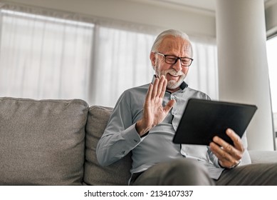 Cheerful Senior Man Having Video Call On Tablet Sitting On The Couch At Home Elderly Man Wearing Eyeglasses Staying In Touch With Friends And Family Using Online Video Call Connecting With People