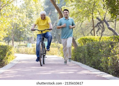 Cheerful senior man riding bicycle  while son running at park
