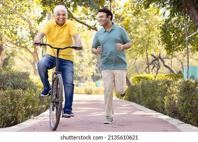 Cheerful senior man riding bicycle  while son running at park
