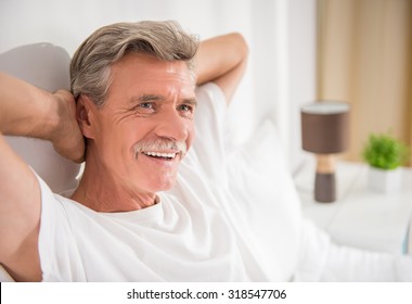 Cheerful Senior Man Is Sitting In Bed And Smiling.