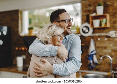 Cheerful senior mother and adult son embracing in the kitchen.