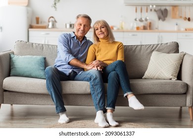 Cheerful Senior Spouses Holding Hands Hugging Sitting On Sofa Smiling To Camera At Home. Front View Of Happy Married Mature Couple Posing On Sofa. Long-Lasting Marriage And Relationship - Powered by Shutterstock