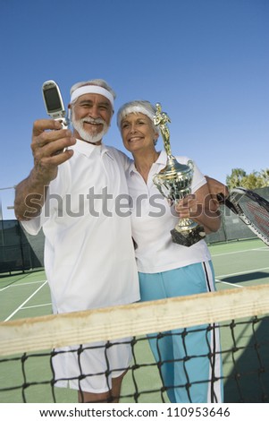Cheerful senior tennis player holding trophy after winning