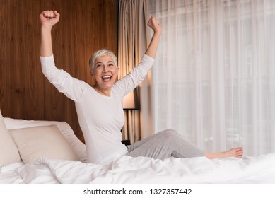 Cheerful Senior Woman With Big Beautiful Smile Getting Ready For Sleep And Stretching In Her Bedroom, Night Routine Concept