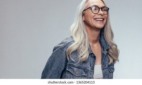 Cheerful Senior Woman In Casuals Looking Away And Smiling Over Grey Background. Happy Mature Woman In Denim Shirt And Eyeglasses.