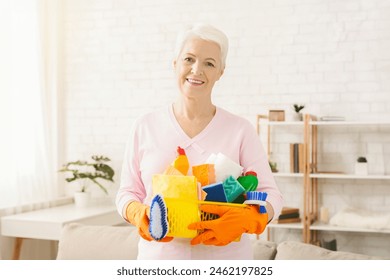 Cheerful senior woman holding a variety of cleaning supplies including a mop, bucket, duster, and spray bottles. She appears to be ready to tackle household chores and maintain cleanliness in home. - Powered by Shutterstock