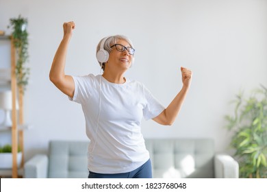 Cheerful Senior Woman Listening To Music In Headphones And Dancing In The Room At Home. 