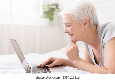 Cheerful Senior Woman Lying In Bed And Watching Something On Laptop, Free Space