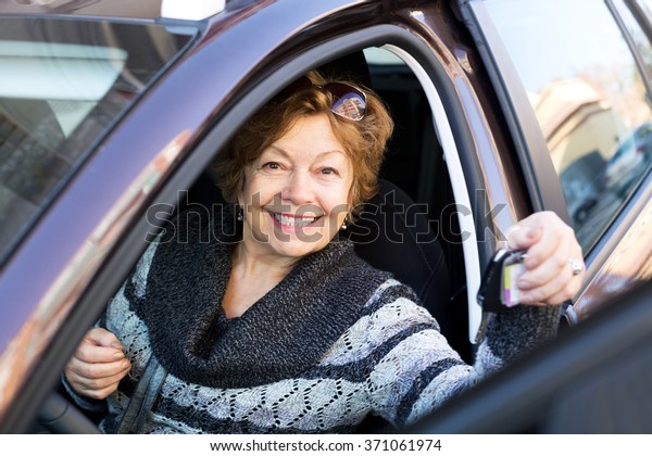 Cheerful\
senior woman sitting in new car at driver\
seat