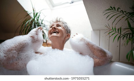 Cheerful senior woman washing in bubble bath tub at home, laughing. - Powered by Shutterstock