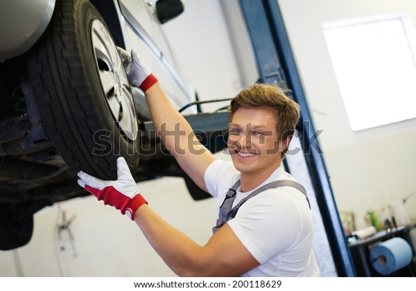 Cheerful serviceman checking suspension in a car\
workshop 