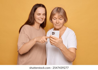 In a cheerful setting, a younger woman excitedly points at a smartphone screen while an older woman looks on with curiosity, highlighting their bond and the joy of sharing experiences. - Powered by Shutterstock