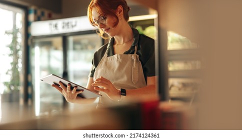 Cheerful shop owner using a digital tablet while standing in her grocery store. Successful female entrepreneur running her small business using wireless technology. - Shutterstock ID 2174124361