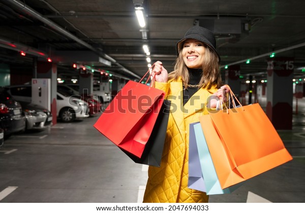 Cheerful shopper woman with purchases walking on\
the parking lot of shopping\
center.