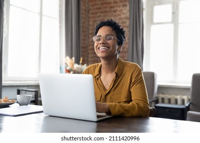 Cheerful short haired African employee sitting at workplace with laptop in office, typing, looking at camera, smiling, laughing. Millennial worker, working business woman in casual head shot portrait - Shutterstock ID 2111420996