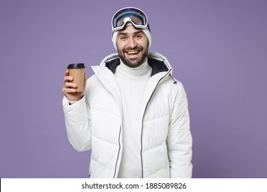 Cheerful Skier Man In White Windbreaker Jacket Ski Goggles Mask Hold Paper Cup Of Coffee Or Tea Spend Extreme Weekend Winter In Mountains Isolated On Purple Background. People Lifestyle Hobby Concept