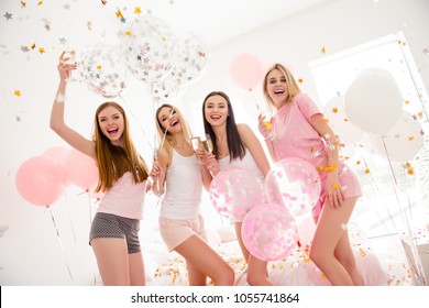 Cheerful slim pretty stylish charming funky girls in night wear in rain of colorful stars, confetti enjoying meeting indoor drinking alcohol laughing standing and looking at camera sleepover party
