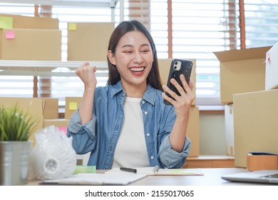 Cheerful small business entrepreneur SME, happy asian young woman owner smile when receive order from customer on app shopping by smartphone, mobile. Merchant online, ecommerce working at home office.