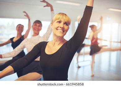 Cheerful Smiling Adult Ballerina Stretching With Hand Up Performing A Dance In Ballet Class.