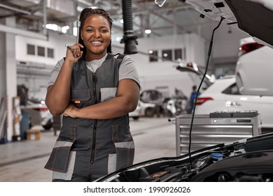 Cheerful smiling afro Female auto repair worker, having a break, looking at camera at repair garage. Woman car mechanician repairs engine of car, wearing overalls uniform. Portrait - Powered by Shutterstock