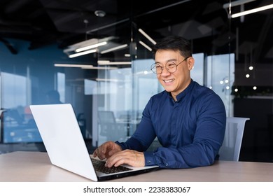 Cheerful and smiling Asian man working inside office, businessman in shirt and glasses using laptop, engineer developer programmer typing code programming software. - Powered by Shutterstock