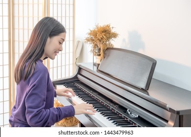 Cheerful Smiling asian young girl playing piano in sost light. Beautiful,happy, joyful, relaxing woman practising piano cheerfully.  - Powered by Shutterstock