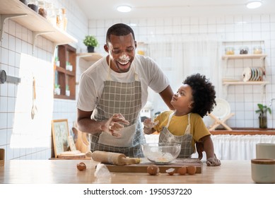 Cheerful Smiling Black Son Enjoying Playing With His Father While Doing Bakery At Home. Playful African Family Having Fun Cooking Baking Cake Or Cookies In Kitchen Together. Single Dad Lifestyle