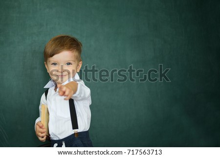 Cheerful smiling boy with books on a green chalkboard background.