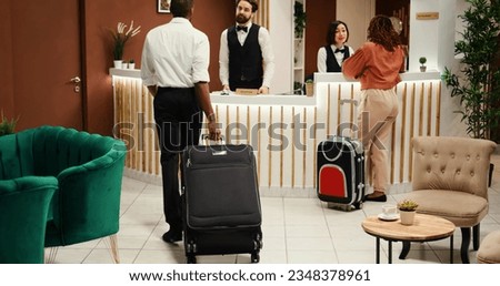Cheerful smiling concierge personnel helping tourists with accommodation booking. Helpful front desk receptionists answering questions about hotel room amenities during check in process