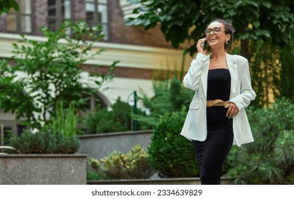 Cheerful, smiling, confident business woman walking outside the office and talking on mobile phone. Concept of business, career development, ambitions, success, office lifestyle - Powered by Shutterstock