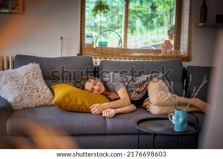 Cheerful smiling curly beautiful young woman lying relaxing on sofa at home, daytime nap