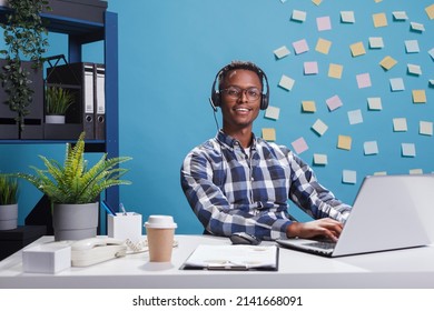 Cheerful Smiling Customer Support Consultant Wearing Headset While In Call With Company Client. Joyful Young Adult Helpline Operator In Conversation With Perplexed Person.