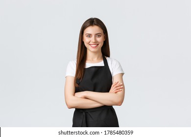 Cheerful Smiling Female Barista In Black Apron Cross Arms Chest, Looking Ready And Confident. Young Girl Employee Open Coffee Shop, Greeting Customers. Saleswoman Running Store