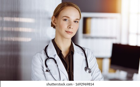 Cheerful Smiling Female Doctor Standing With Arms Crossed In Clinic. Portrait Of Friendly Physician Woman. Medicine Concept