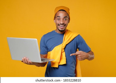 Cheerful Smiling Funny Young African American Man Wearing Casual Blue T-shirt Hat Standing Pointing Index Finger On Laptop Pc Computer Isolated On Bright Yellow Colour Background Tattoo Translate Life