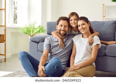 Cheerful smiling happy family sitting on the floor in the living room at home with their child girl and looking at camera. Cute daughter hugging her parents on sofa. Love and family leisure concept. - Powered by Shutterstock