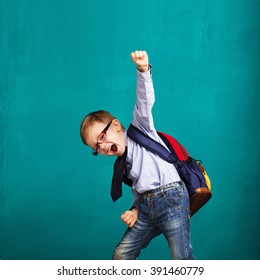 Cheerful smiling little boy and big backpack jumping   having fun against blue wall  Looking at camera  School concept  Back to School