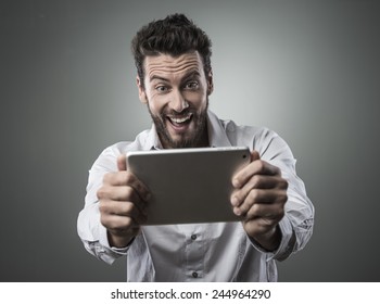 Cheerful Smiling Man Watching Videos And Playing Video Games On His Tablet