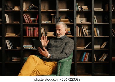 Cheerful smiling mature adult male greeting and waving hand, talking by digital tablet. Aged man alone at home has video call on tablet to keep in touch with family during isolation. - Powered by Shutterstock